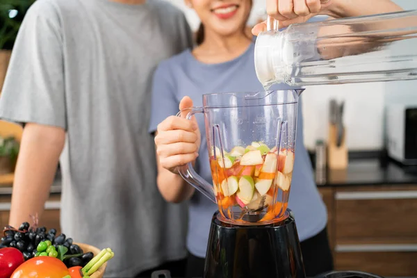Happy Asian couple enjoys rinsing fresh water in blender machine for making healthy vegan smoothie on the kitchen counter. Couple making vegan smoothie together at home for a healthy lifestyle.