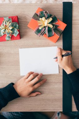 Bir adamın elinin en üst görüntüsü boş bir Noel kartpostalına kalemle yazmaktır. Noel tatili boyunca eve sürpriz hediyeler göndermek için birlikte oturup yılbaşı kartı yazan çift..