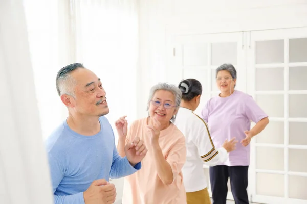 Active Asian senior group mix with man and woman exercise by dancing together at home with relaxing, smiling and laughing. Indoor activity for mature seniors and retirement people. Focus on senior man