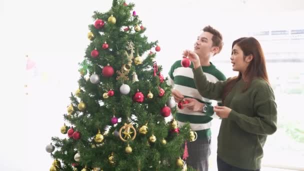 一对快乐的年轻夫妇穿着毛衣 在家里客厅的圣诞树上装饰各种浴盆 很开心 享受并庆祝圣诞佳节 实时4K视频 — 图库视频影像