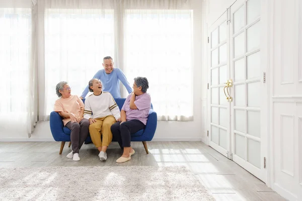 The group of happy and healthy three Asian senior women sits together on a sofa with an Asian senior man standing in the back. Smiling and laughing together. Image with copy space
