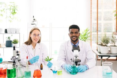 Kafkas ve siyah tebessümlü bilim adamlarının portreleri ve bir araştırma laboratuarındaki kameraya bakın. Laboratuvarda kenevir bitkisi ve marihuana üzerinde çalışan bir grup kimya öğrencisi.