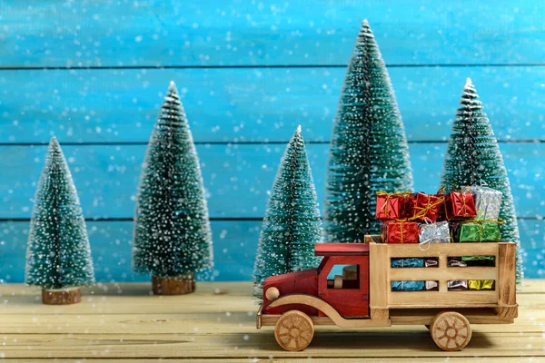 Noel hediyeleri Noel Baba şapkasıyla Noel ağaçlarının yanında Tahta bir masada kar yağarken. 