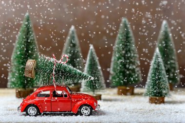 Tahta bir masada kar yağarken çatıda köknar ağaçlarının yanında Noel ağacı olan kırmızı oyuncak bir araba. Noel ve Yeni Yıl kutlaması kavramı.