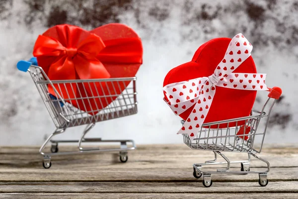 Kırsal ahşap bir masada, içinde kalp şeklinde hediye kutuları olan iki alışveriş arabası. Satışlar ve alışveriş konsepti.