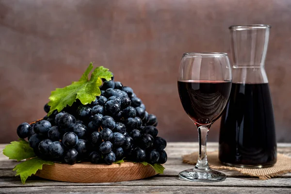 Cam sürahi ve kırmızı şarap kadehi ve ahşap masada taze üzüm..