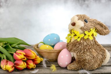 Paskalya yumurtası boyalı, tüylü ve ahşap arka planda turuncu-sarı laleli samandan yapılmış komik bir tavşan. Paskalya konsepti.