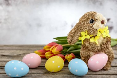 Paskalya yumurtaları boyanmış samandan yapılmış komik bir tavşan ve ahşap zemin üzerinde turuncu-sarı laleler. Paskalya konsepti.