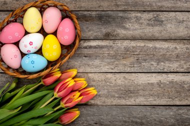 Renkli Paskalya yumurtaları sepeti ve ahşap bir masada bir buket lale. Paskalya konsepti.