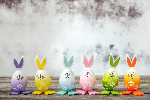 Bir grup Paskalya yumurtası şirin tavşan suratlı ve tahta bir masada tavşan kulaklı. Paskalya konsepti.