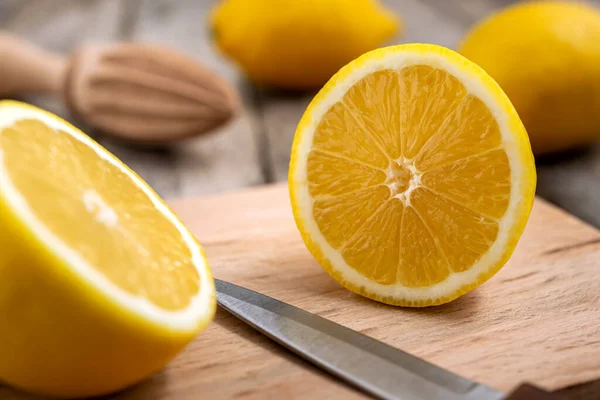 Fresh lemon cut in half with knife on wooden cutting board.