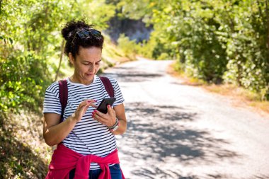 Woman tourist use navigation on the smartphone while hiking on summer sunny day.