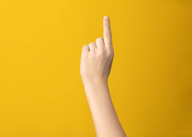 Female hand gesture shows one index finger on yellow background isolated 