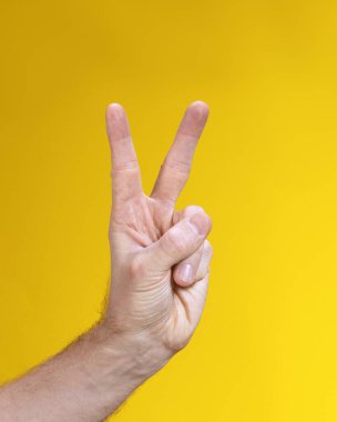 Sarı arka planda iki el hareketi yapan bir erkek. Zafer işareti, V sumbol.