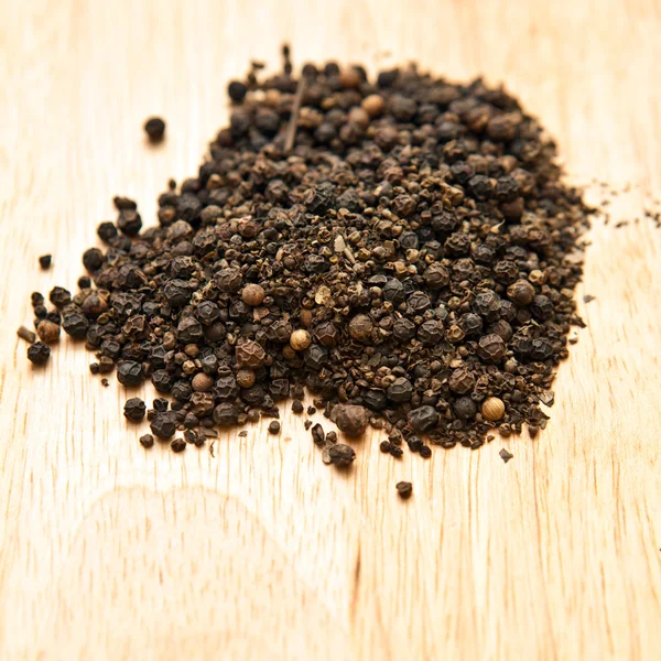 Guisantes de pimienta negra en una tabla de madera — Foto de Stock