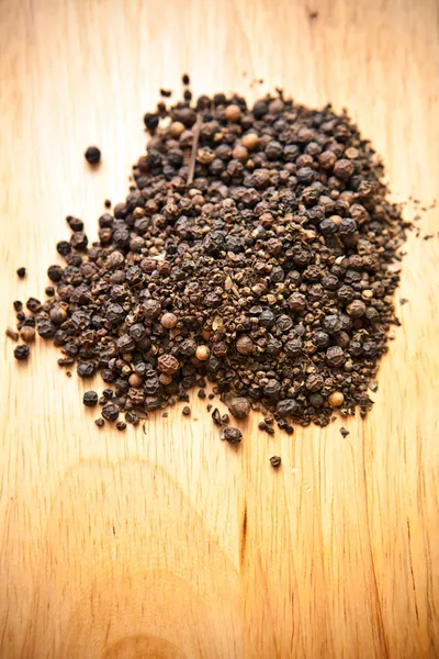 Guisantes de pimienta negra en una tabla de madera — Foto de Stock