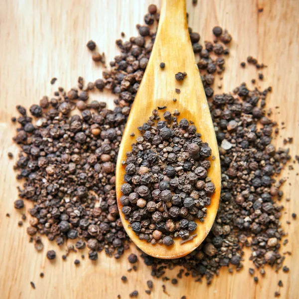 Guisantes de pimienta negra en una cuchara de madera — Foto de Stock