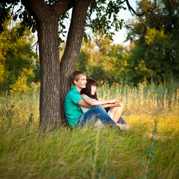 Jeune couple amoureux assis sous un arbre — Photo