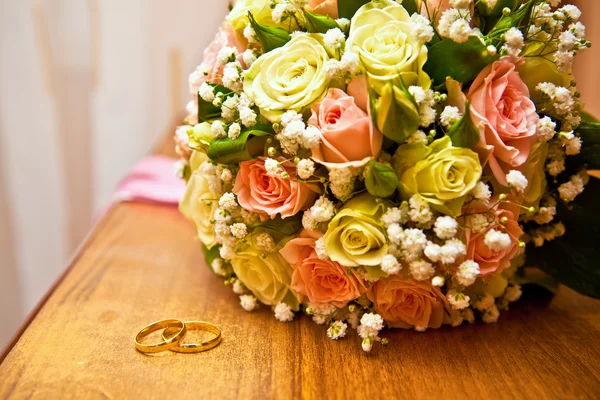 Zlaté prsteny vedle svatební kytice — Stock fotografie