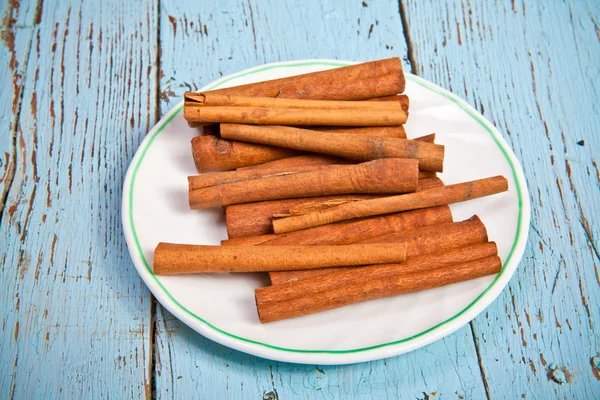 Bastoncini di cannella su un piatto su uno sfondo di legno — Foto Stock