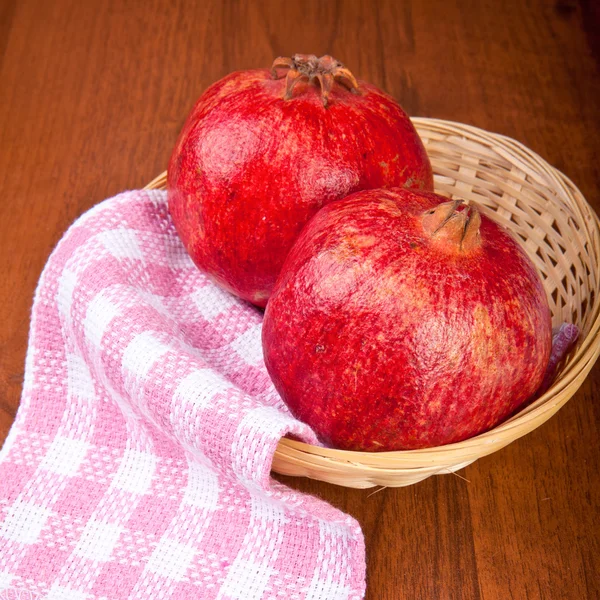 Pomegranate fruit in a wicker basket on a wooden table — Stock Photo, Image