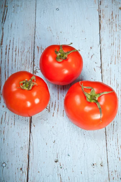 Três tomates em um fundo de madeira — Fotografia de Stock