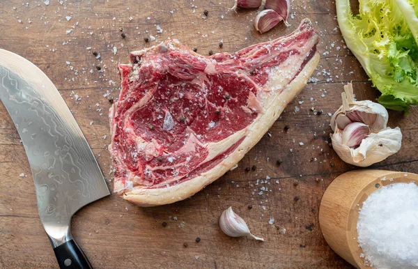 Tahta bir tahtanın üzerinde çiğ rubia gallega bifteği. Bıçak, yeşil salata ve deniz tuzu taneleri, biber, sarımsak ile tatlandırılmış.