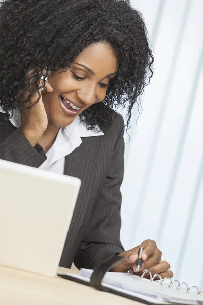 Mujer afroamericana usando teléfono celular y computadora portátil en la oficina —  Fotos de Stock