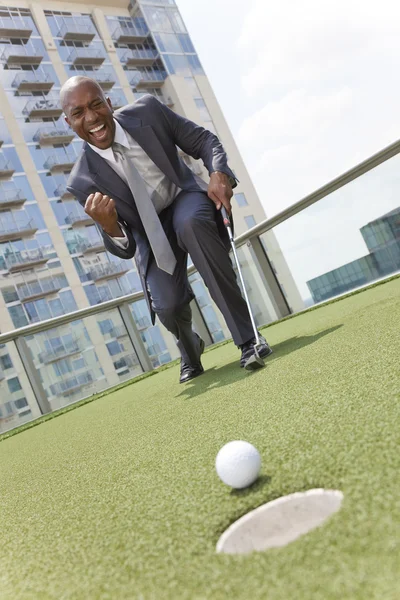 Hombre de negocios afroamericano jugando al golf en la azotea de rascacielos — Foto de Stock