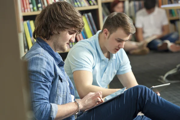 Estudantes do sexo masculino usando computadores tablet na biblioteca — Fotografia de Stock
