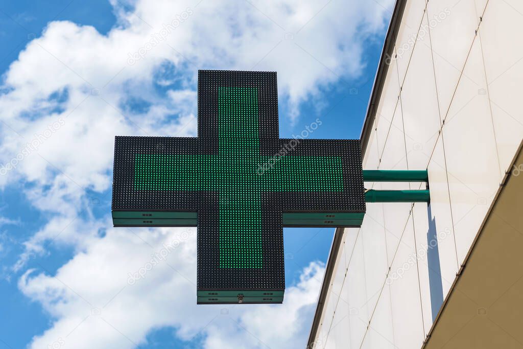 A green cross sign for a pharmacy hangs on the building. Against the background of the sky with clouds
