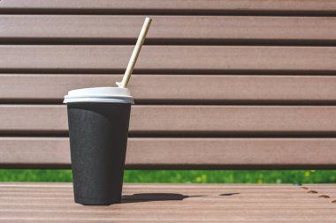 Kahveli bir kağıt bardak sokakta bir bankta duruyor.