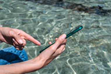 Telefonun önündeki kızın parmağı. Tatil köyünün suyunun zeminine karşı