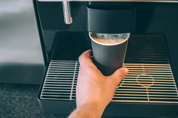 The guy pours coffee from the coffee machine into a paper cup