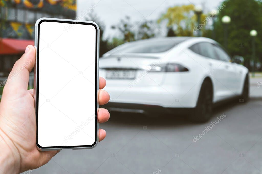 Smartphone mockup in the hands of a man. Against the background of a white electric car