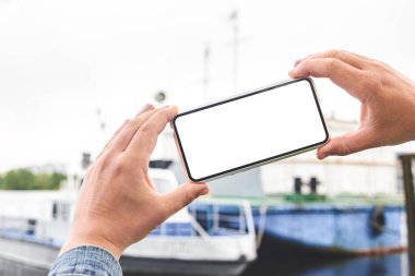 Akıllı telefon modeli, bir adamın ellerindeydi. Körfezin arka planında yatlar var.