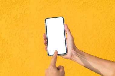 Bir kızın elindeki akıllı telefonun bir maketinin önündeki parmak izi gibi. Dekoratif alçıdan yapılmış sarı bir cephede. Yakın plan.
