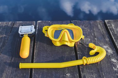 Sarı yüzgeçli su geçirmez kamera ve şnorkelle dalmak için maske, ahşap iskelede dalmak için. Bulutların yansımasıyla mavi suyun arka planına karşı