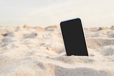 Telefonunu kuma koy. Deniz suyunun arka planına karşı. Plajda rahatlama konsepti