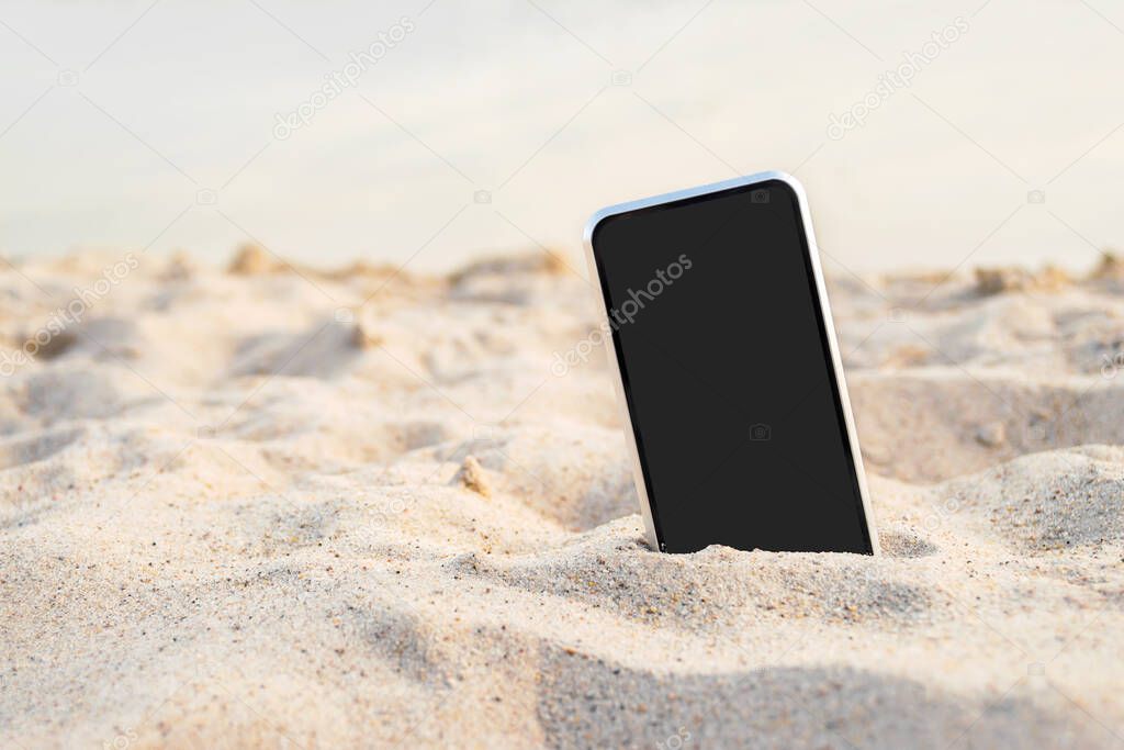Phone in the sand. against the backdrop of sea water. The concept on the theme of relaxation on the beach