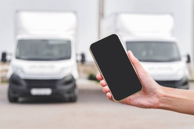 Bir kadının elinde telefon. Kamyonların arka planına karşı. Lojistik kavramı