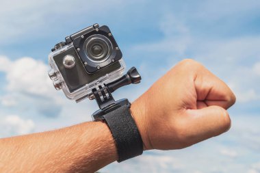 Yakın plan, bir adamın elinde aksiyon kamerası. Arkaplanda bulutlu mavi bir gökyüzü