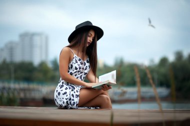 Nehrin kenarında yürüyen, köprüde oturan, kitap okuyan bir kız.