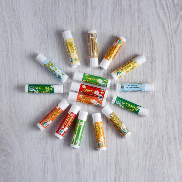 Kamianets-Podilskyi, Ukrayna, 7 Mart 2022: Sierra Bees dudak kremleri açık ahşap masanın üzerinde daireler çiziyor. Işık arka planında organik bal mumu dudak kremi.. 