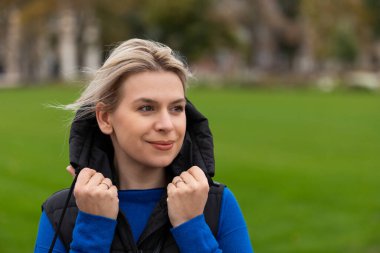 Rüzgârlı havada yeleğini tutan sarışın beyaz kadın portresi, başka tarafa bakıyor. 