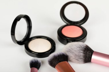 Beyaz arkaplanda makyaj fırçaları olan gül sarısı allık ve fosforlu kalem resmini kapat