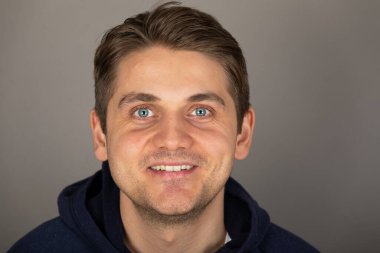 Gri arkaplan önünde kameraya bakan mavi gözlü yakışıklı sarışın bir adamın portresi.  