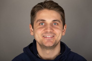 Gri arkaplan önünde kameraya bakan mavi gözlü yakışıklı sarışın bir adamın portresi.  