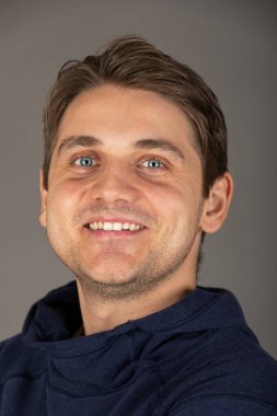 Gri arkaplan önünde kameraya bakan mavi gözlü yakışıklı sarışın bir adamın portresi.  