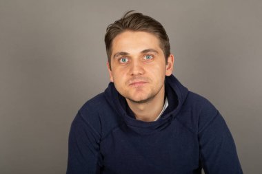 Gri arkaplan önünde kameraya bakan mavi gözlü yakışıklı sarışın bir adamın portresi.   